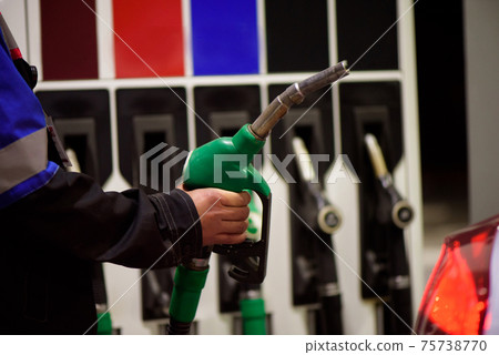Gas station worker in workwear refueling luxury car with gasoline holding filling gun at the station Gas station worker in workwear refueling luxury car with gasoline holding filling gun at the station 75738770