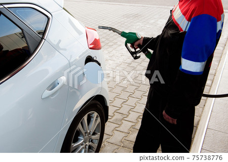 Gas station worker in workwear refueling luxury car with gasoline holding filling gun at the station 75738776