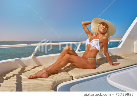Young woman on the deck of a boat in open sea at sunny summer day Young woman on the deck of a boat in open sea at sunny summer day 75739985