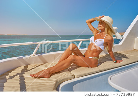 Young woman on the deck of a boat in open sea at sunny summer day Young woman on the deck of a boat in open sea at sunny summer day 75739987
