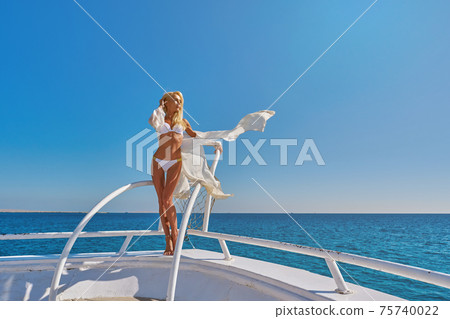 Young woman standing on the deck of a boat in open sea at sunny summer day 75740022