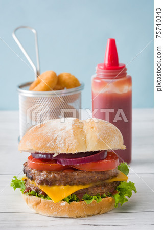 Cheeseburger with beef,tomato, lettuce, onion and onion rings on wooden table Cheeseburger with beef,tomato, lettuce, onion and onion rings on wooden table 75740343