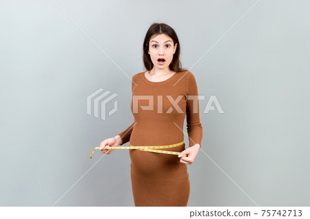 pregnant woman measuring her growing abdomen at colored background. Inch tape measure. Copy space 75742713