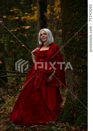Halloween concept, glamorous costume detail. Young beautiful and mysterious woman in woods, in white Dress and Red Cloak. Little red hood or vampire story Halloween concept, glamorous costume detail. Young beautiful and mysterious woman in woods, in white Dress and Red Cloak. Little red hood or vampire story 75743093