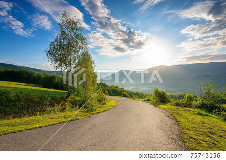 countryside road in mountains on a sunny day. beautiful view in to the distant foggy valley from the top of the pass. trees along the way. wonderful rural landscape in summer 75743156