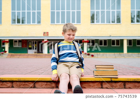 Portrait of Beautiful school boy looking happy outdoors at the day time. Sitting on the steps with books and a large school backpack school theme. 75743539