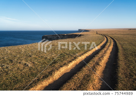 A gravel road leading toward horizon. Spectacular view on the sea and blue sky in the evening. Panoramic image A gravel road leading toward horizon. Spectacular view on the sea and blue sky in the evening. Panoramic image 75744989