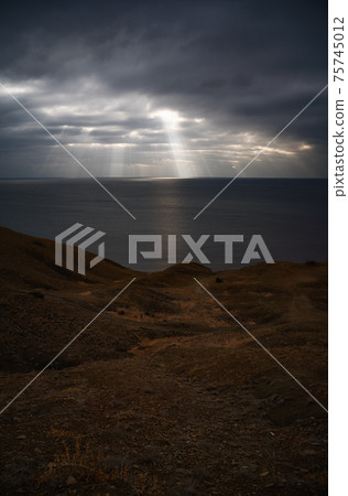 Sun rays make their way through dramatic clouds. Weather turns bad in the evening. Beautiful seascape. Vertical image Sun rays make their way through dramatic clouds. Weather turns bad in the evening. Beautiful seascape. Vertical image 75745012