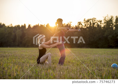 Pilates trainer correcting a trainee while in a pose holding dumbbells 75746273