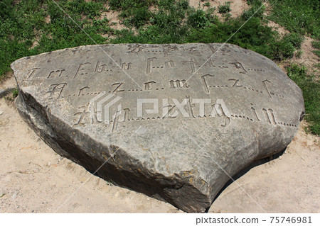Encoded ancient engraved inscription by Gothic font with missing letters on a large boulder 75746981