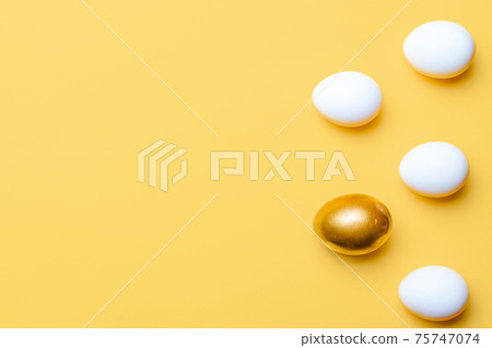 Easter holiday. Golden, white colour egg on pastel yellow background in Happy Easter decoration. Spring holiday top view with copy space. 75747074