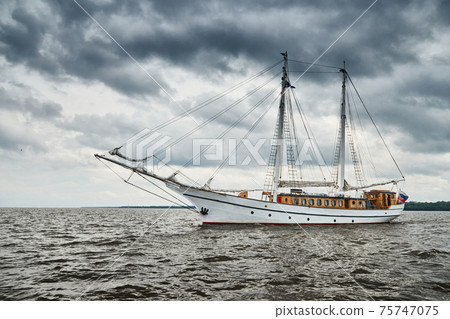 Antique sailing frigate of white color to the sea, the lowering storm sky, sails are lowered, masts and ropes 75747075