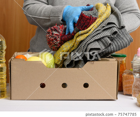 woman in gloves keeps collecting food, fruits and things and a cardboard box for helping those in need woman in gloves keeps collecting food, fruits and things and a cardboard box for helping those in need 75747785