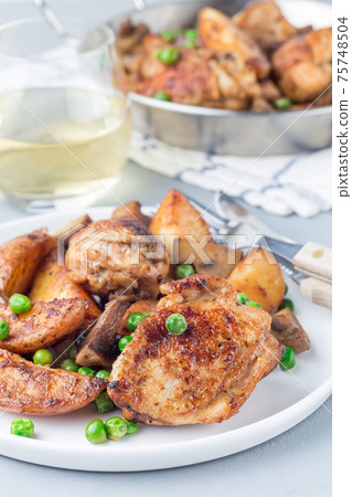 Chicken with potatoes, mushrooms and green peas, on a white plate and in metal pot, vertical Chicken with potatoes, mushrooms and green peas, on a white plate and in metal pot, vertical 75748504