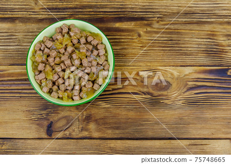 Canned food for cats or dogs in green ceramic bowl on wooden floor. Top view 75748665