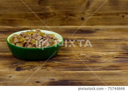 Canned food for cats or dogs in green ceramic bowl on wooden floor 75748666