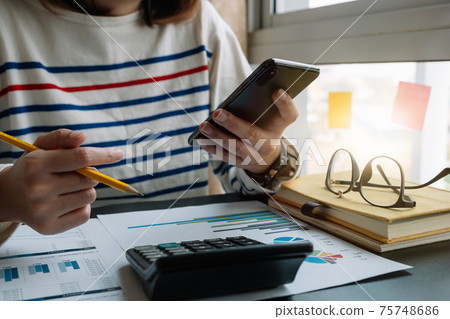 Close up of accountant hand holding smartphone while working on calculator to calculate financial data report,  75748686