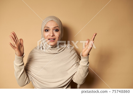 Arabic Muslim woman wearing traditional clothing and covered head in hijab gesturing with hands and expressing anger and frustration Arabic Muslim woman wearing traditional clothing and covered head in hijab gesturing with hands and expressing anger and frustration 75748860