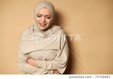 Young Muslim woman in hijab suffering from abdominal pain Young Muslim woman in hijab suffering from abdominal pain 75748863