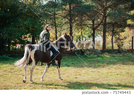 On a warm autumn day, a young girl went out to ride her mare on horseback around the farm On a warm autumn day, a young girl went out to ride her mare on horseback around the farm 75749443