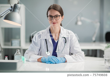 A woman doctor with glasses at her desk in the office is ready to receive patients of the clinic. A spacious office of the public hospital 75749608