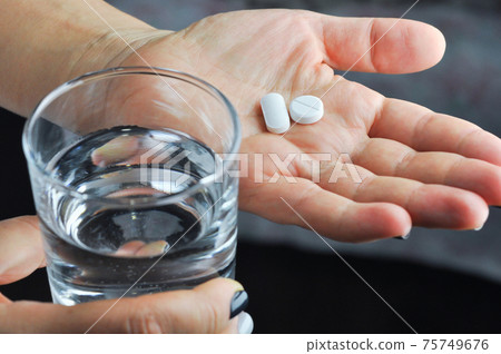Hands with tablets and glass of water. 75749676