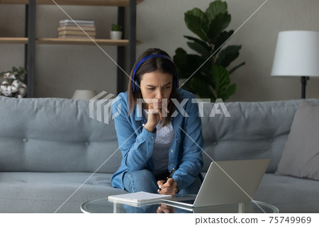 Focused woman wearing headphones looking at laptop screen, taking notes Focused woman wearing headphones looking at laptop screen, taking notes 75749969