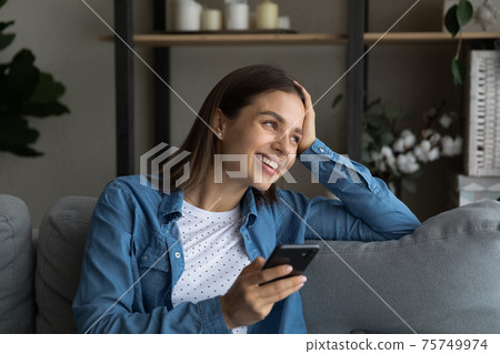 Close up smiling woman distracted from phone, sitting on couch Close up smiling woman distracted from phone, sitting on couch 75749974