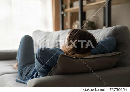 Rear view calm woman relaxing, lying on couch at home 75750064