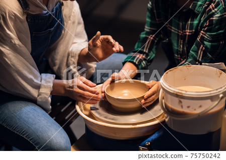 a young woman potter helps a cute boy to make a gift for his mother out of clay. 75750242