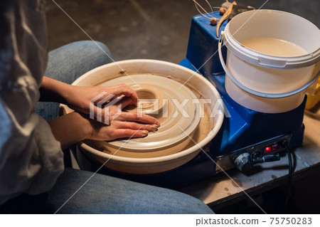 master class on sculpting a pot in an art workshop. the girl behind the potter's wheel makes a blank with her hands. 75750283