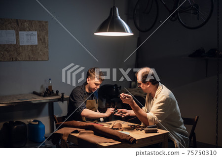 an experienced shoemaker and his assistant in their workshop make shoes from leather to order. 75750310