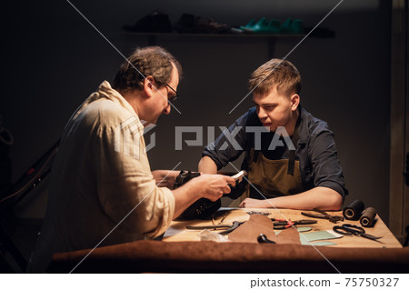 an elderly shoemaker and his apprentice create shoes by hand in their workshop with various tools. 75750327