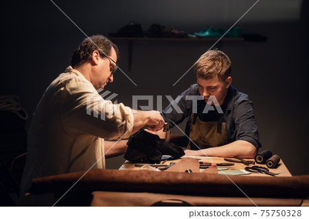 an experienced shoemaker and his assistant in their workshop make shoes from leather to order. 75750328