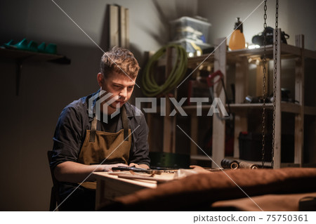 a young apprentice makes blanks for the production of shoes in the workshop. 75750361