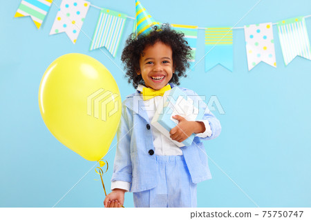 Adorable ethnic kid with birthday present and balloon in hands 75750747