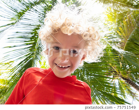 Beach fun. Curly boy under palm tree. 75751549