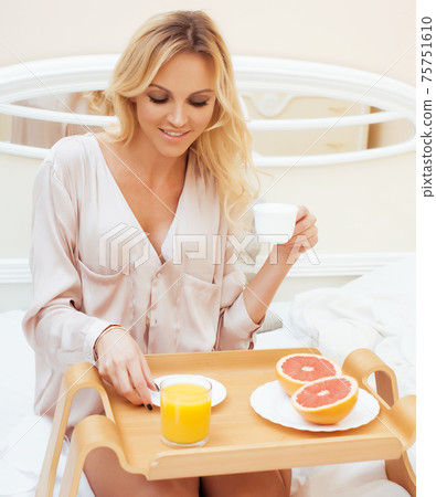 young beauty blond woman having breakfast in bed early sunny morning, princess house interior room 75751610