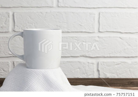 Household utensils, a white cup stands on a napkin against the background of a kitchen stone brick wall of a milky shade, the concept of clean dishes Household utensils, a white cup stands on a napkin against the background of a kitchen stone brick wall of a milky shade, the concept of clean dishes 75757151