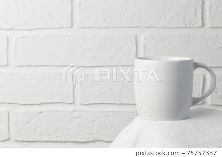 Household utensils, a white cup stands on a napkin against the background of a kitchen stone brick wall of a milky shade, the concept of clean dishes Household utensils, a white cup stands on a napkin against the background of a kitchen stone brick wall of a milky shade, the concept of clean dishes 75757337