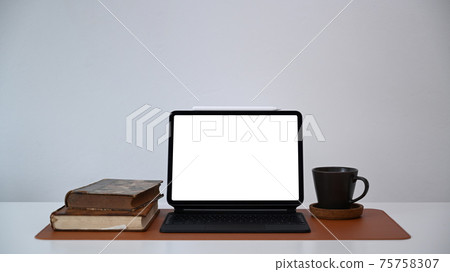 Front view of computer tablet, books and coffee cup on white office desk. Front view of computer tablet, books and coffee cup on white office desk. 75758307