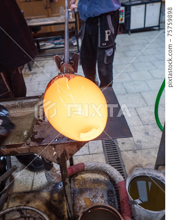 Worker in a glass studio. Talented glassblower is forming hot glass piece 75759898