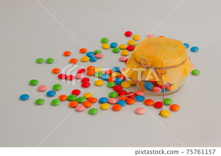 Chocolate candies, small multi-colored in a jar with a bow. 75761157