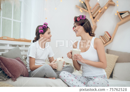 Woman and girl in curlers with cups communicating Woman and girl in curlers with cups communicating 75762528