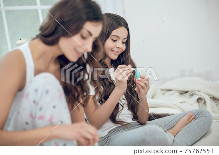 Girl sitting with open bottle of nail polish Girl sitting with open bottle of nail polish 75762551