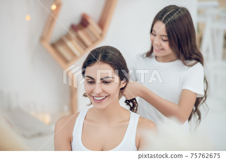 Joyful cute mom and daughter doing her hair Joyful cute mom and daughter doing her hair 75762675