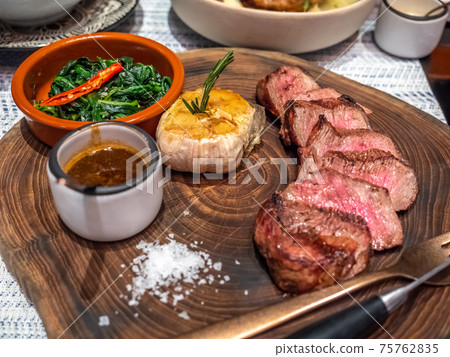 Angus beef steak served with garlic, gravy sauce and spinach in Mediterranean style restaurant Angus beef steak served with garlic, gravy sauce and spinach in Mediterranean style restaurant 75762835