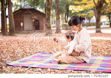 父母和孩子在秋天公園玩智能手機 75763107