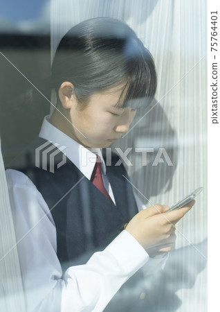 Junior high school students looking at their smartphones by the window (image of request to refrain from going out) Junior high school students looking at their smartphones by the window (image of request to refrain from going out) 75764401