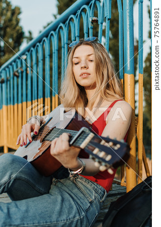 Creative hobbies, guitar lessons, playing musical instruments. Acoustic guitars for beginners. Young blonde woman with Acoustic guitar outdoor Creative hobbies, guitar lessons, playing musical instruments. Acoustic guitars for beginners. Young blonde woman with Acoustic guitar outdoor 75764891